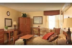 A cozy bedroom with warm tones, featuring a bed, a wooden wardrobe, and a small table by the window.
