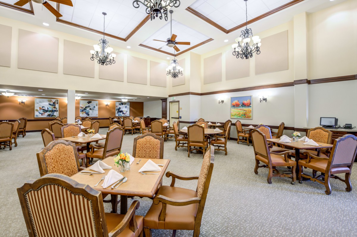 A spacious dining room with elegant chandeliers and wooden furniture set up for dining.