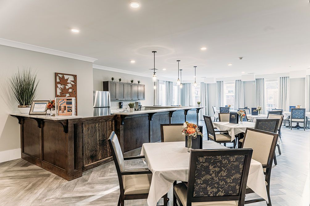 A modern dining area with neatly arranged tables and chairs, adjacent to a kitchen space with stylish lighting.