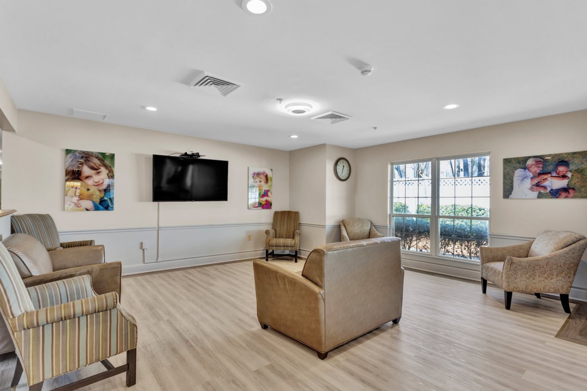A cozy living room with seating, a television, and large windows allowing natural light.
