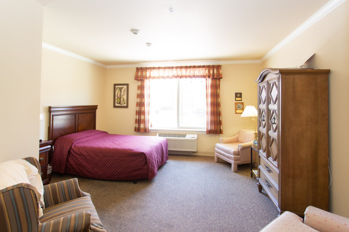 A spacious hotel room featuring a bed, armchair, and decorative furniture.