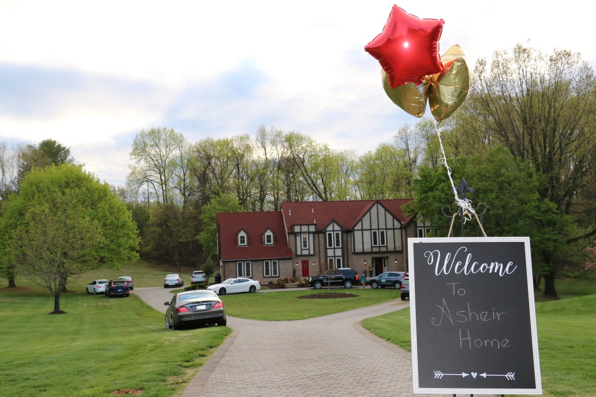 A charming house with a driveway adorned by balloons and a welcome sign, surrounded by lush trees.