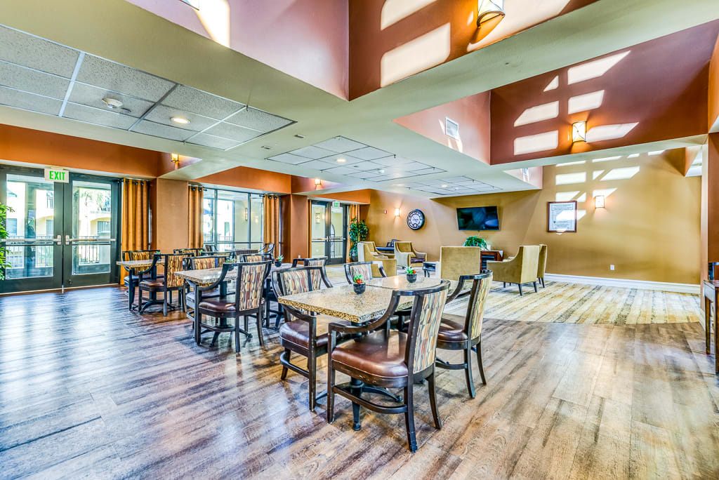 A spacious dining area with ample natural light, featuring several tables and chairs on a wooden floor.