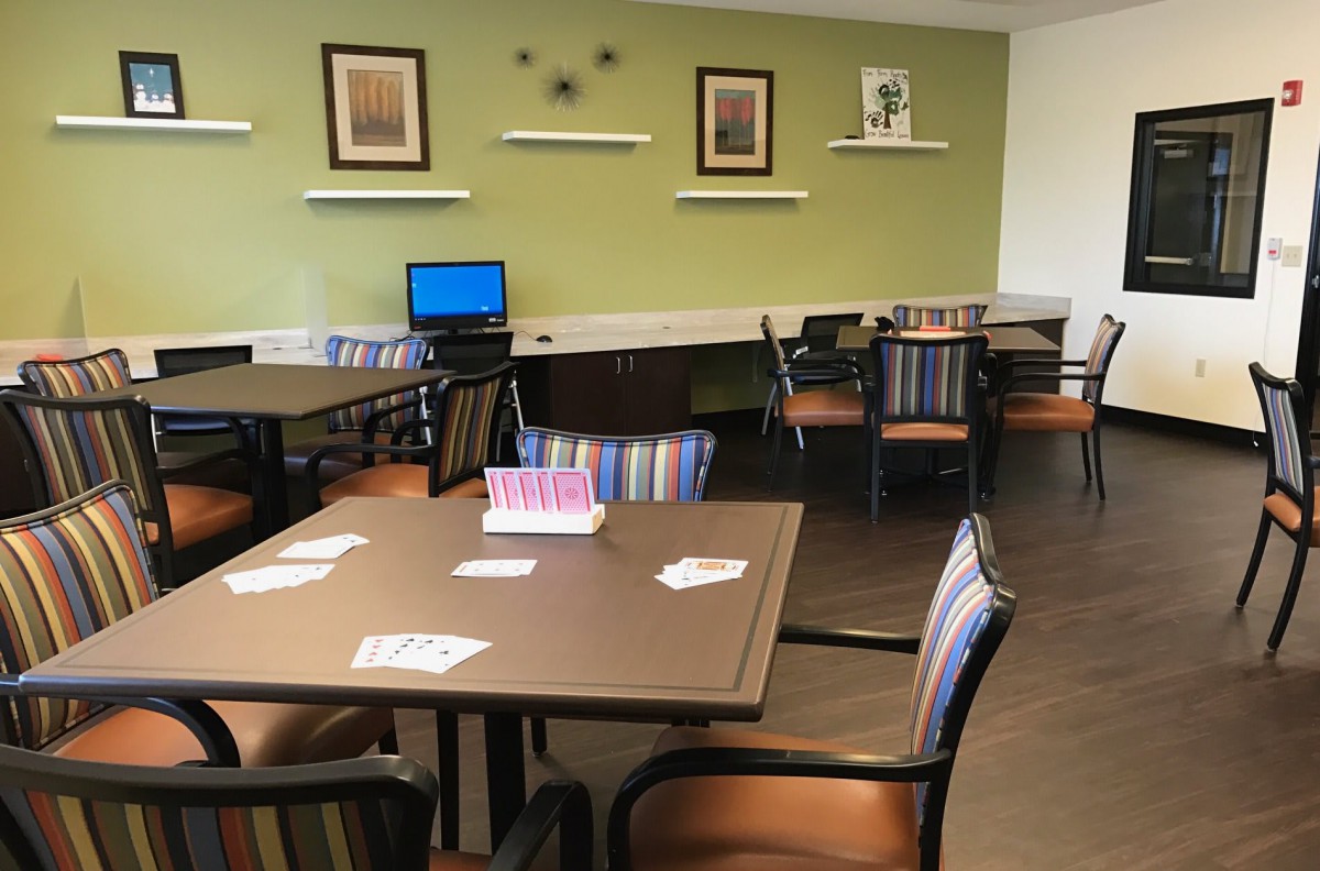 A cozy library reading area featuring tables, chairs, bookshelves, and a computer station.