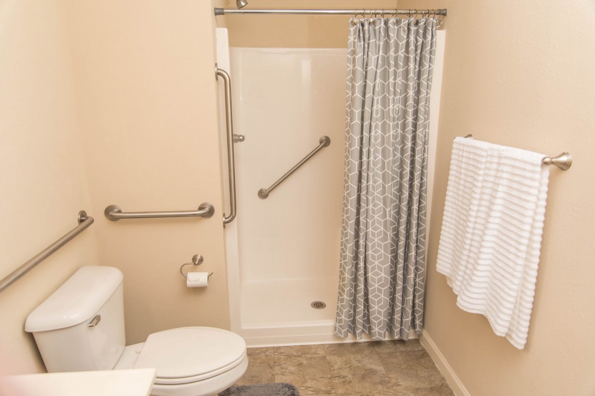 An accessible bathroom with a shower, grab bars, toilet, and towels.