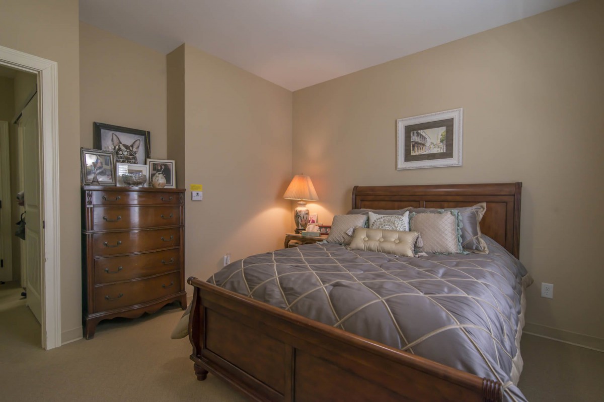 A cozy bedroom with a wooden bed and dresser, softly illuminated by a bedside lamp.