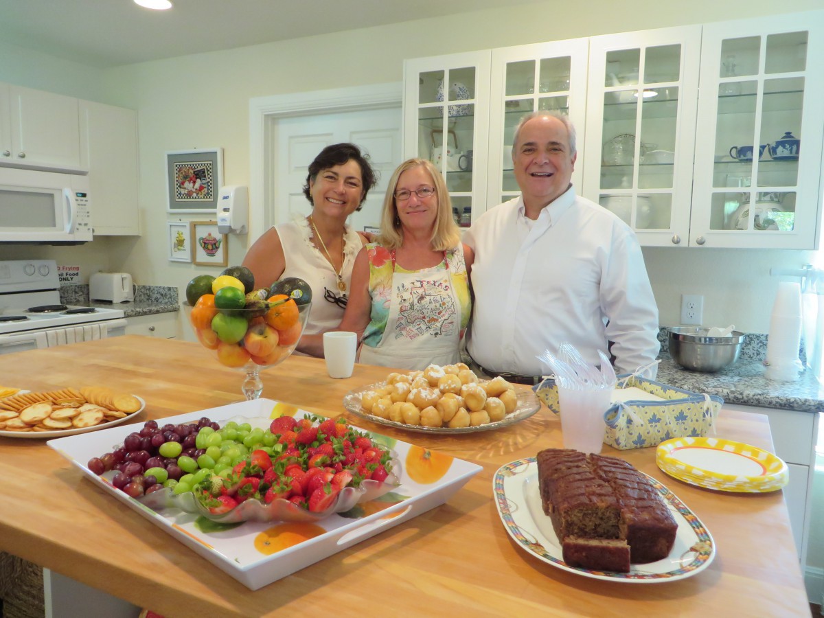 Three people in a kitchen enjoying a spread of fruits and baked goods.