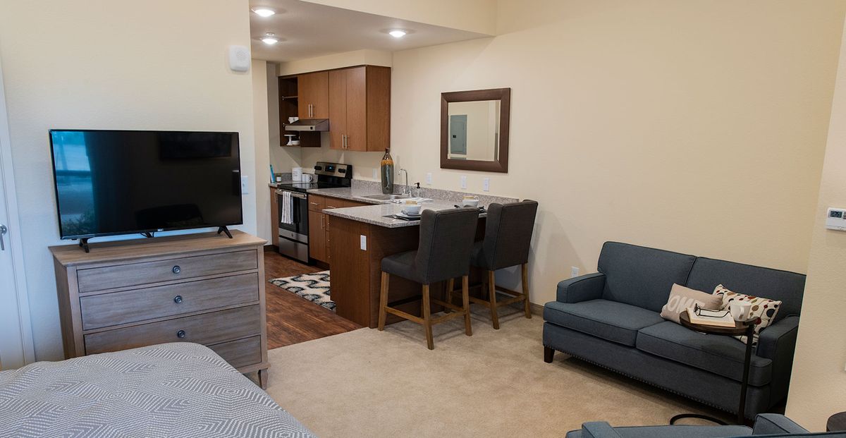 A cozy open-concept apartment with a kitchen and living area featuring bar stools and modern furniture.