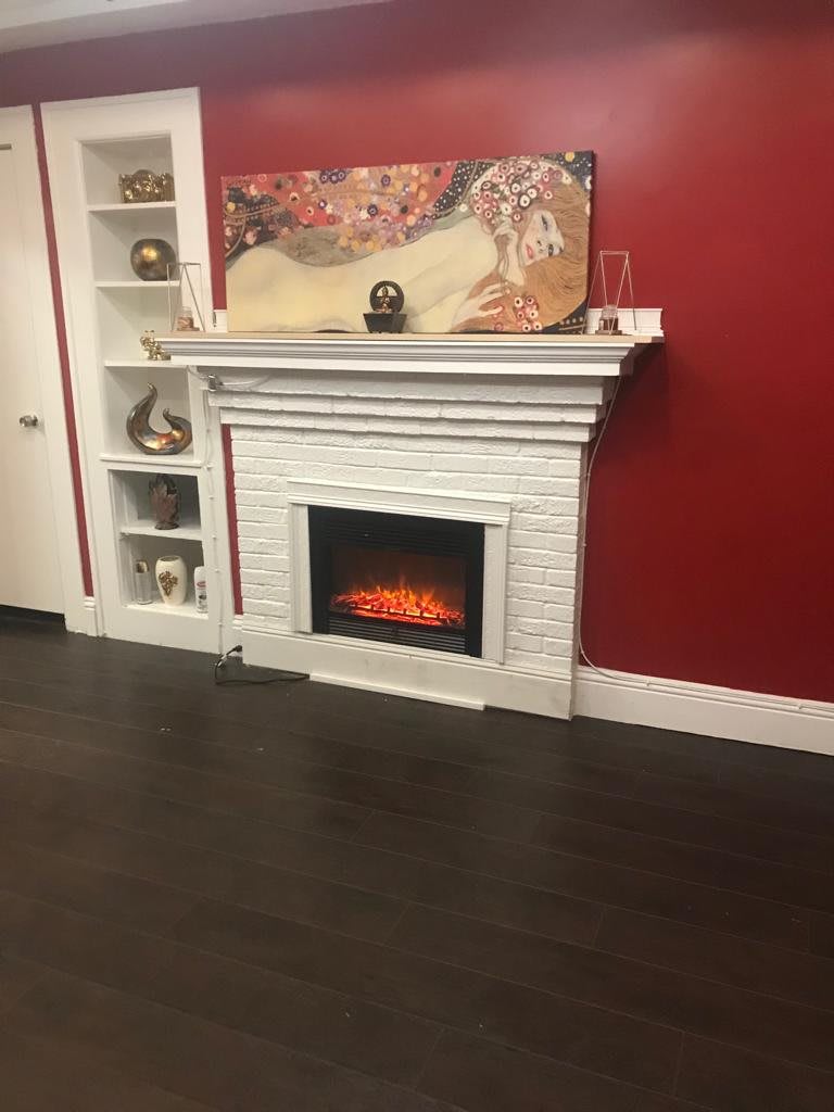 A cozy living room featuring a decorative fireplace set against a bold red wall, with shelves displaying various ornaments.