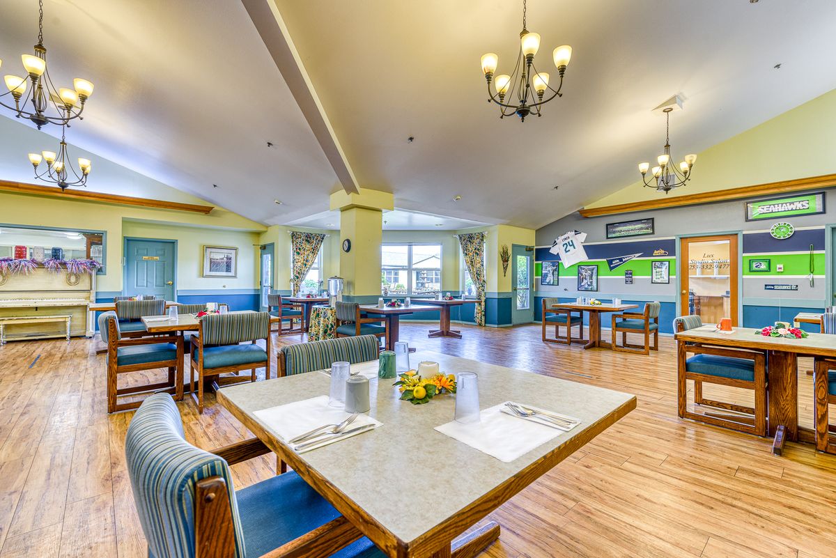 A well-lit and spacious dining area in a senior living facility, featuring neatly arranged tables and comfortable seating.