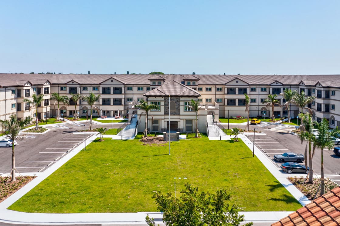 A modern apartment complex with manicured lawns and palm trees on a clear day.
