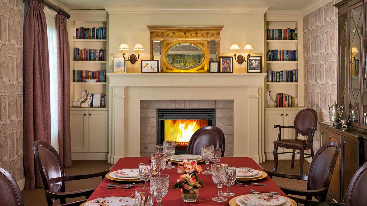 An elegant dining room with a cozy fireplace, surrounded by bookshelves and set for a formal dinner.