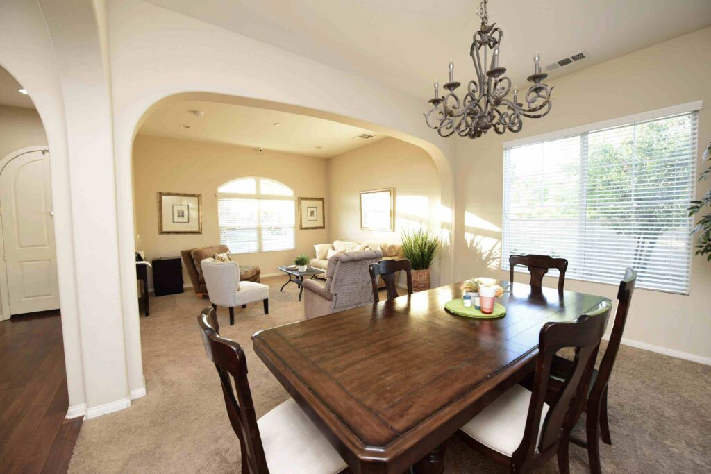 A cozy dining and living area featuring a wooden table, elegant chairs, and a decorative chandelier.