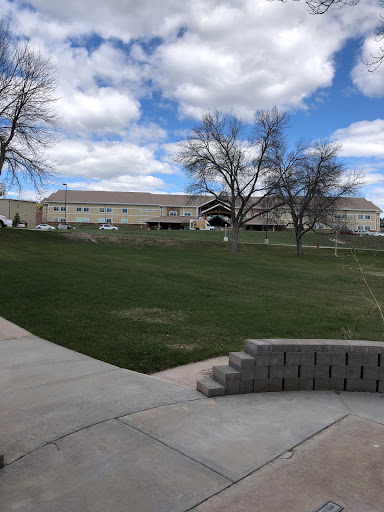 A serene park with lush green grass and a cloudy sky, featuring buildings in the background.