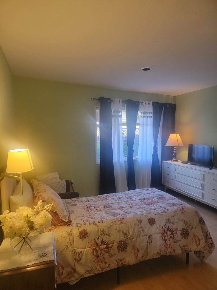 A cozy bedroom with warm lighting, featuring a neatly made bed, curtains, and a dresser.
