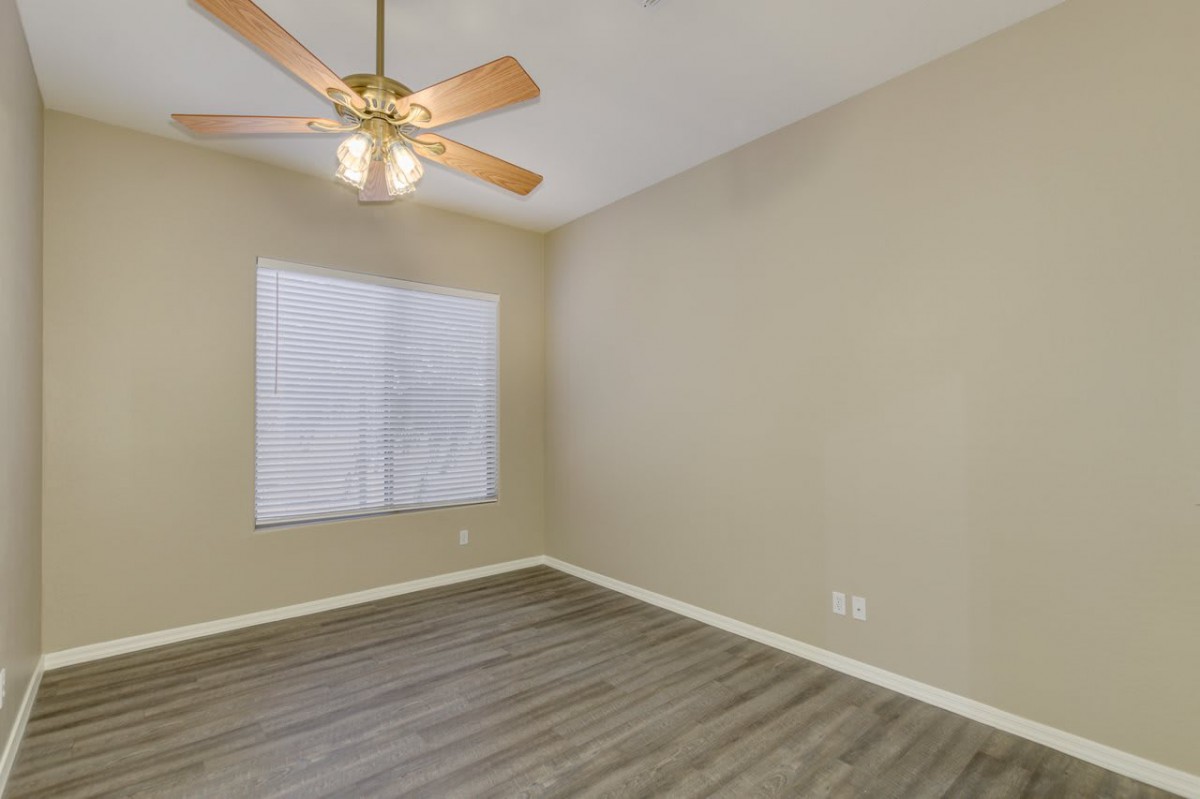 An empty room with a ceiling fan and hardwood flooring.