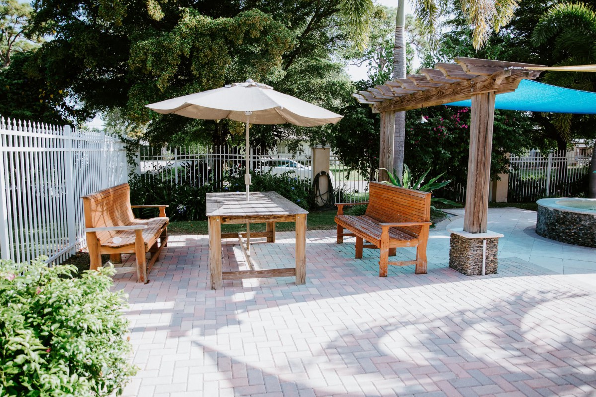 A cozy outdoor patio area with wooden furniture and an umbrella, surrounded by lush greenery.