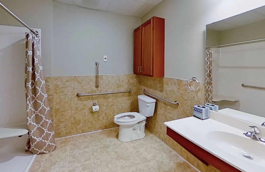 An accessible bathroom featuring a toilet, sink, and safety grab bars.