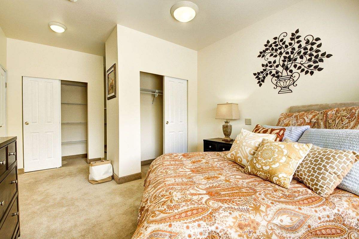 A cozy and elegantly decorated bedroom featuring a large bed with patterned bedding, a nightstand with a lamp, and an open closet area.