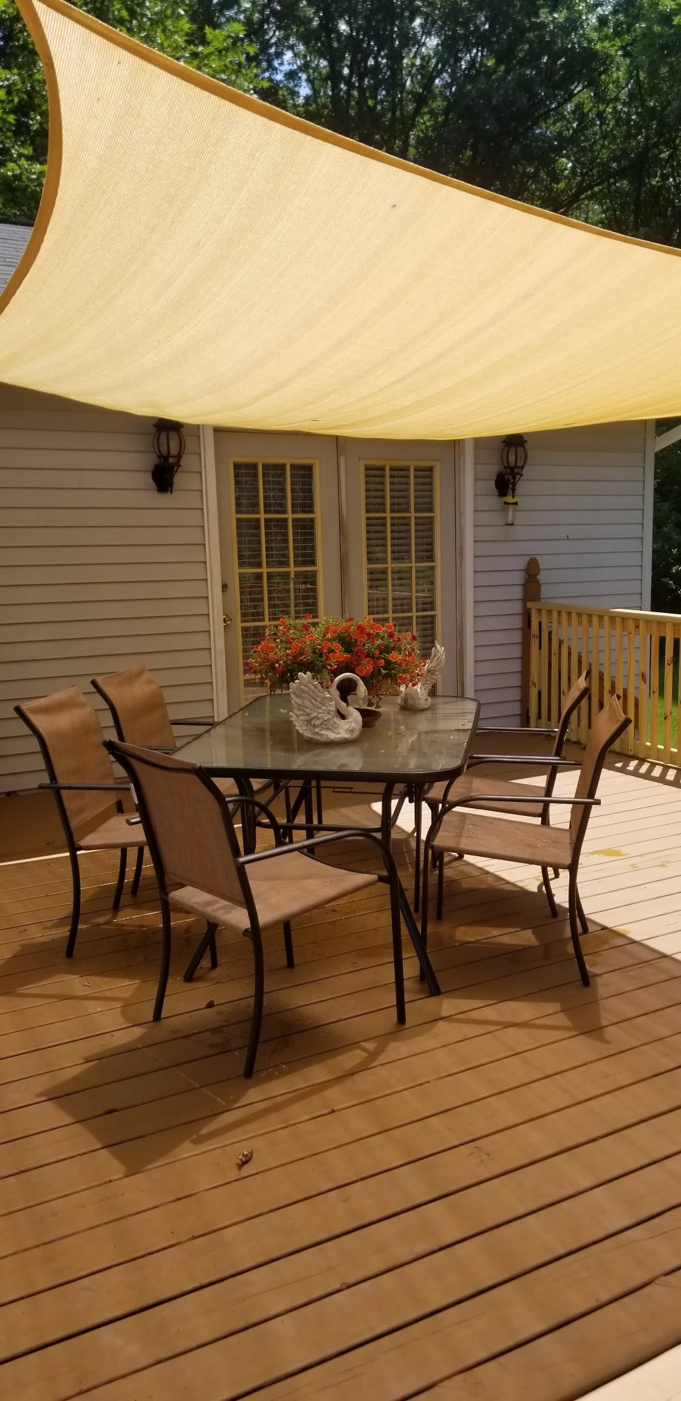 A cozy outdoor patio with a glass table and chairs under a sunshade.