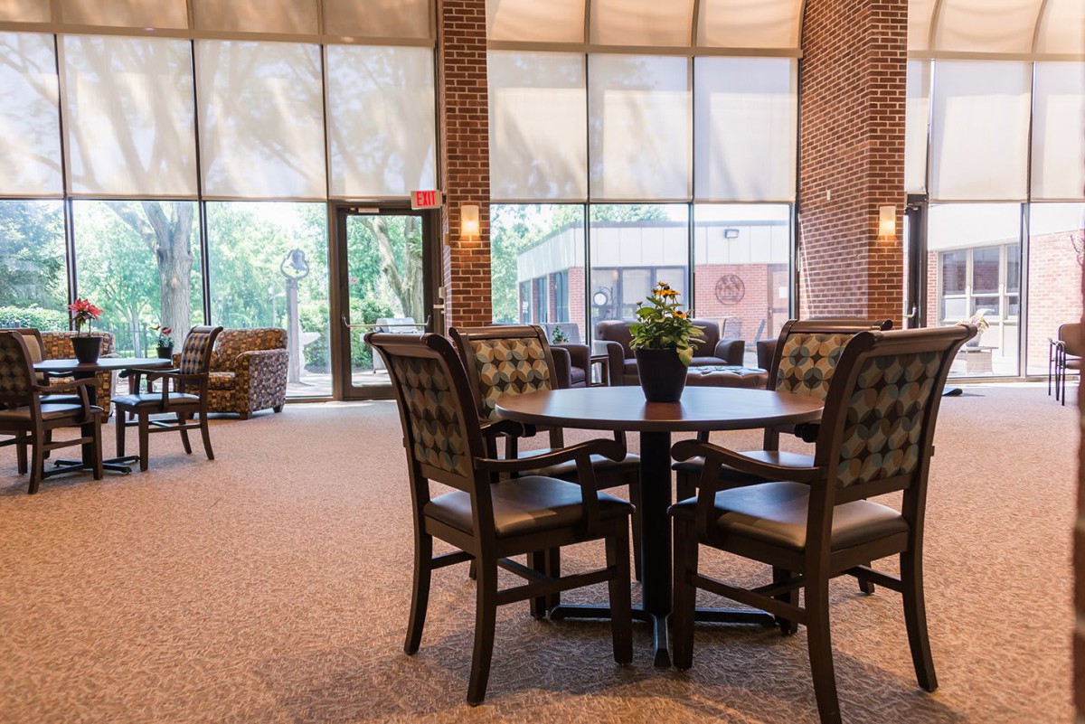 A spacious lobby area with a table and chairs, illuminated by natural light streaming through large windows.