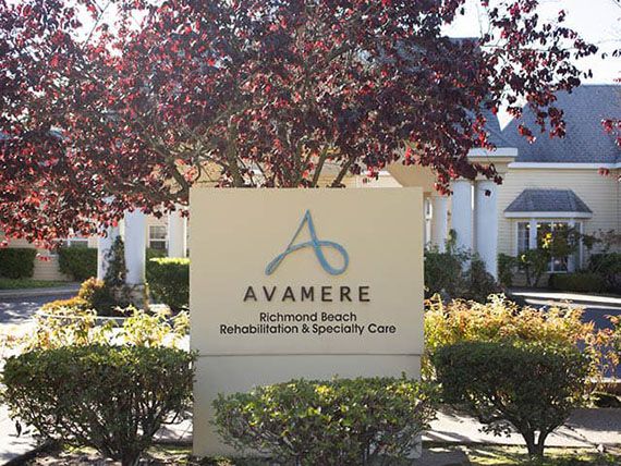 A sign for Avamere Post-Acute Rehab, set against a backdrop of trees and greenery.