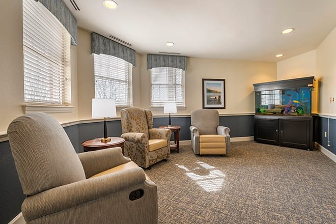 A cozy living room with comfortable armchairs, large windows, and a fish tank.