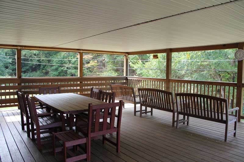 A covered porch with wooden furniture overlooking a lush green view.
