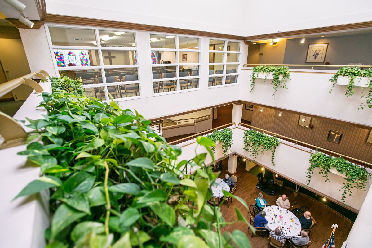 An indoor atrium with plants, balconies, and a dining area filled with people.