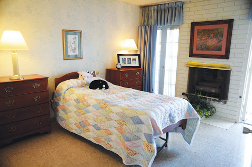 A cozy bedroom featuring a single bed with a colorful quilt, a sleeping cat on the bed, and warm lighting.