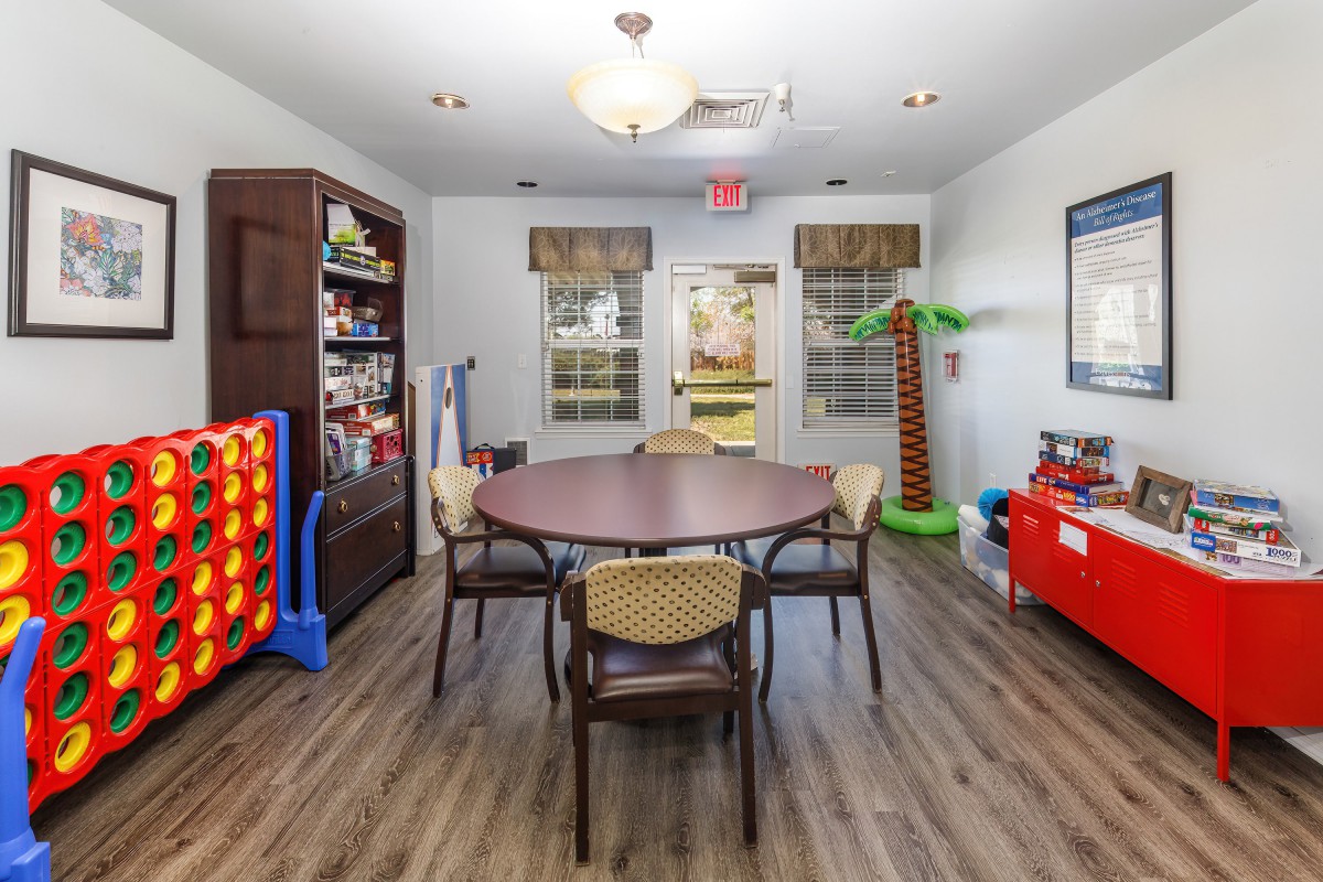 A children's playroom with a round table surrounded by chairs, shelves filled with toys, and games set up for play.
