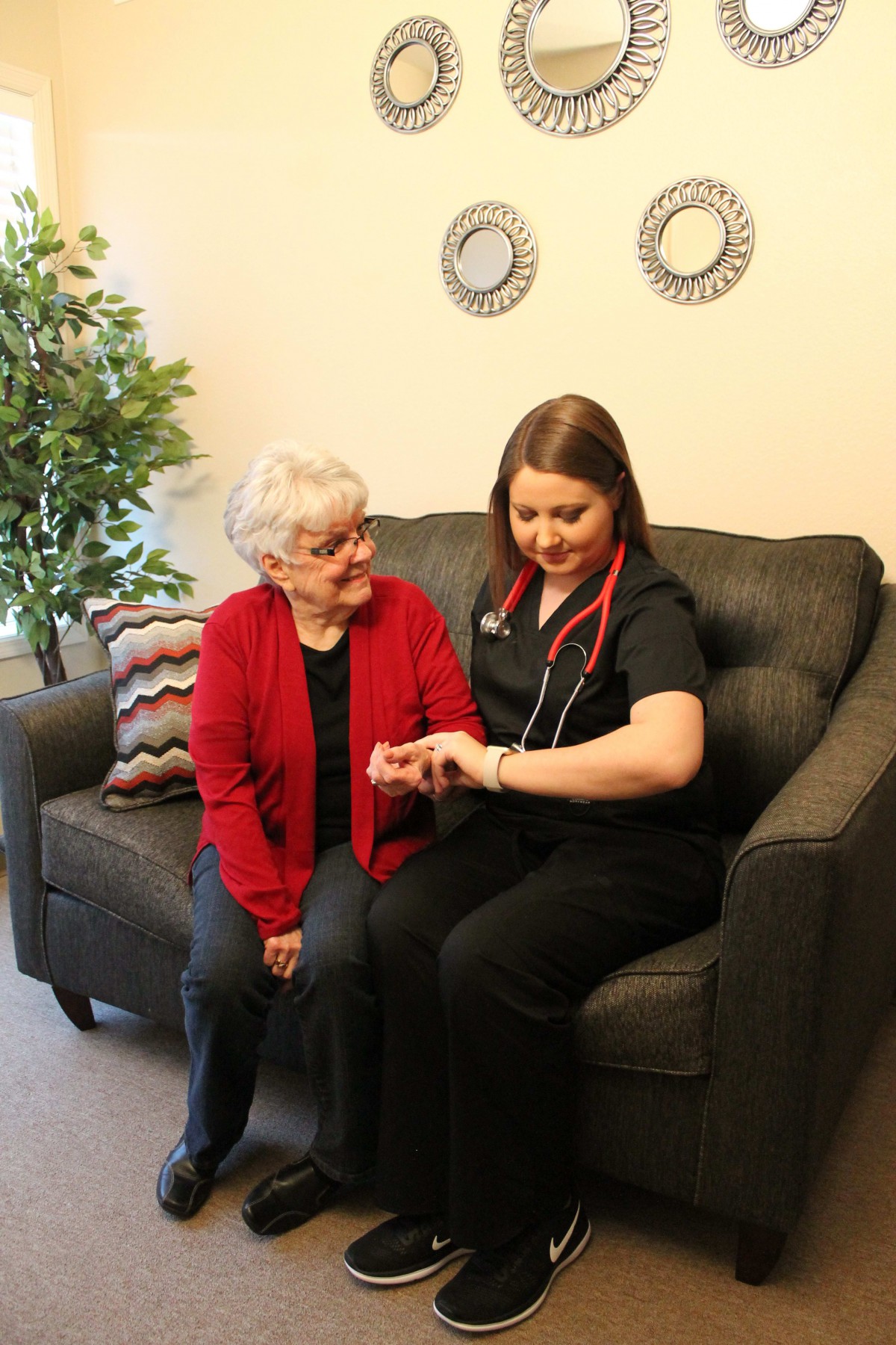 A caregiver or nurse is assisting an elderly woman in a living room setting, providing healthcare services.
