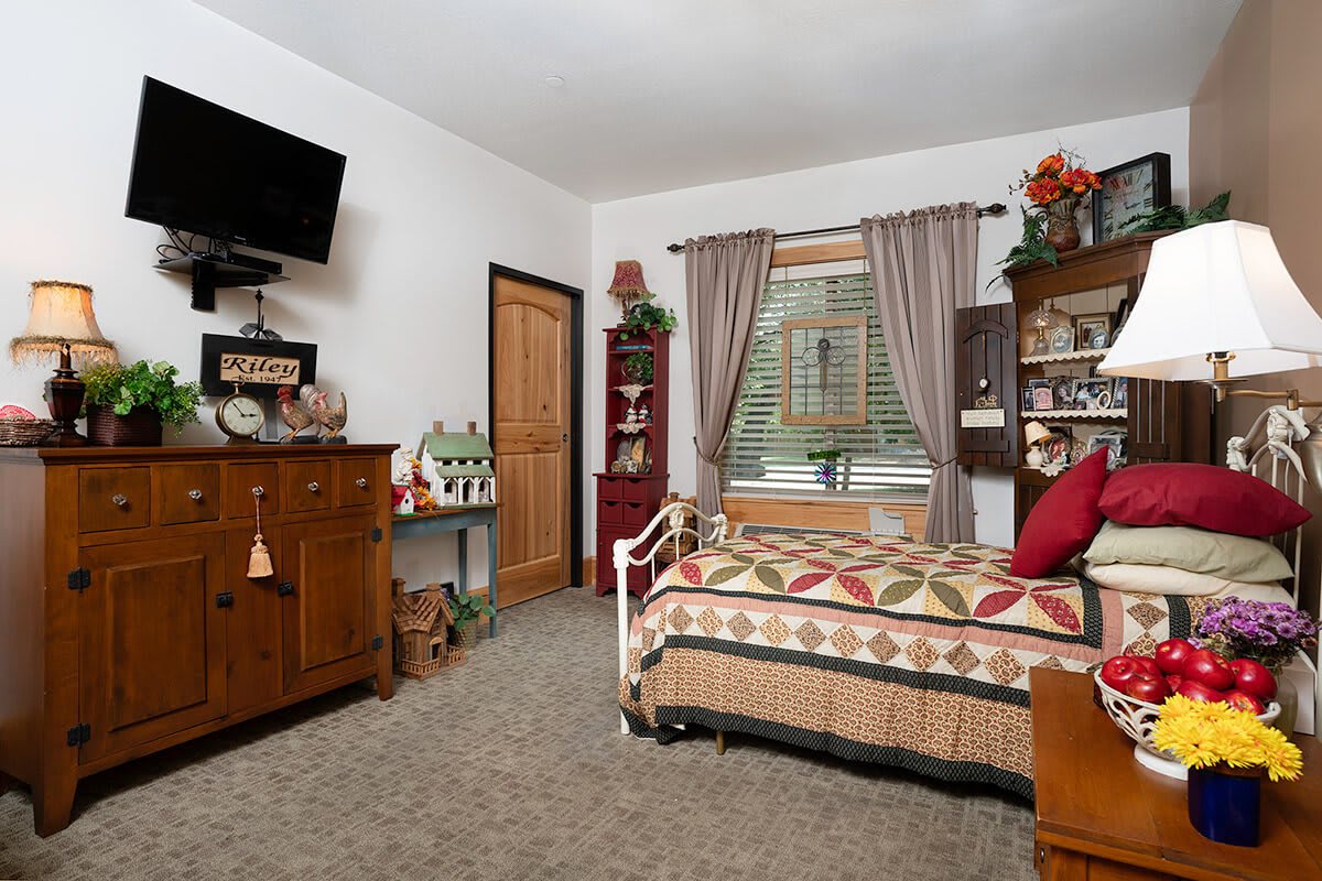 A cozy bedroom featuring traditional decor with a daybed adorned with a quilt, wooden furniture, and a wall-mounted TV.
