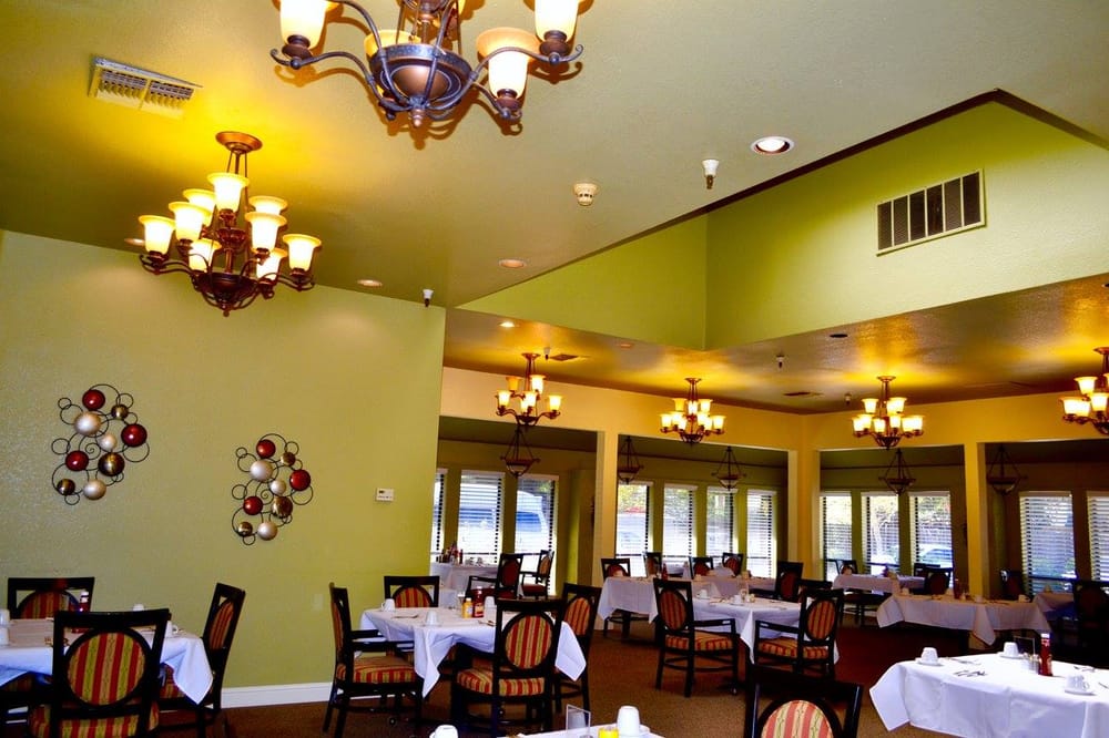 A well-lit restaurant interior with elegant chandeliers hanging above neatly arranged tables and chairs.