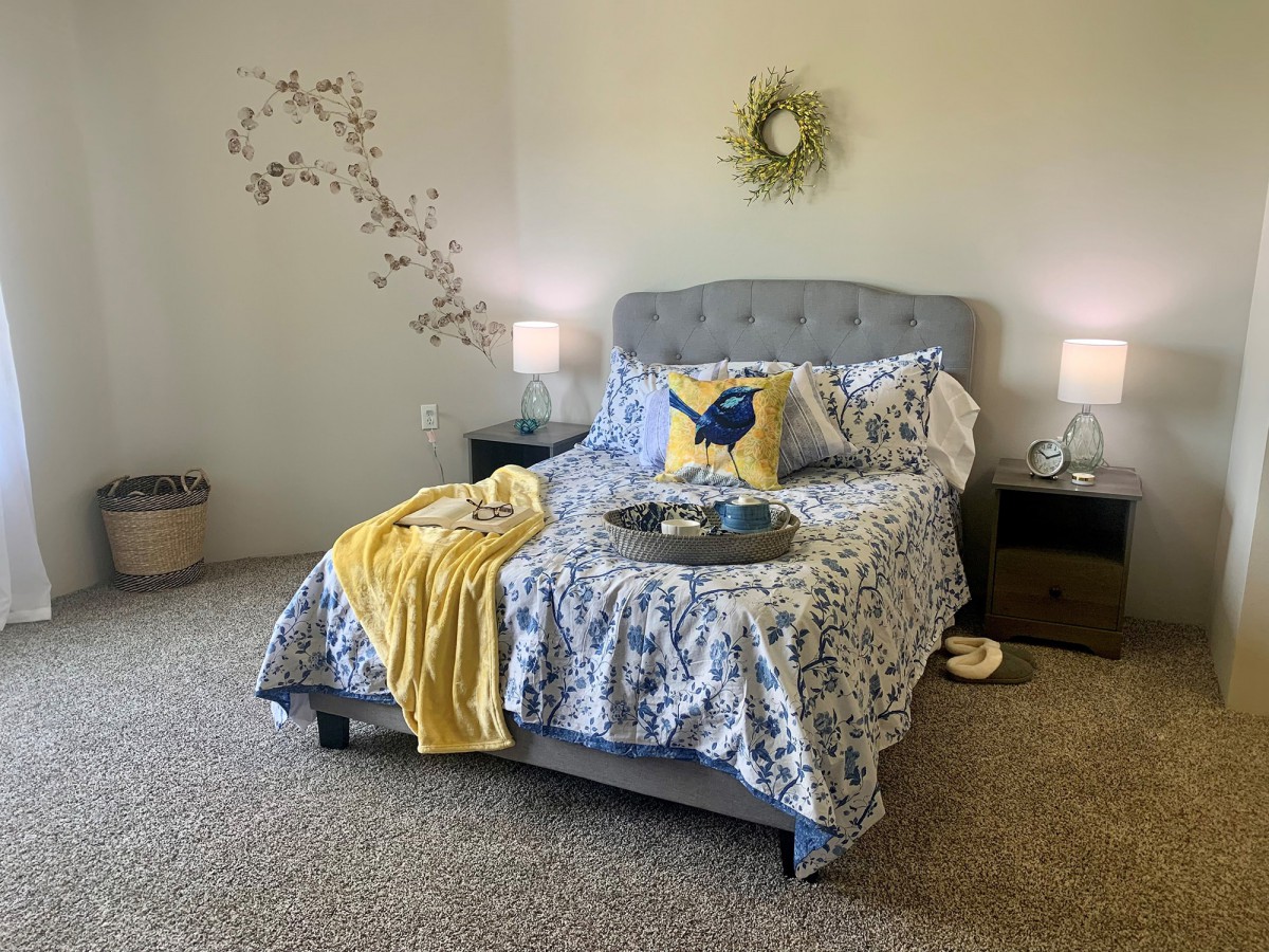 A cozy bedroom with a neatly made bed featuring blue and yellow bedding, decorative pillows, and bedside lamps.