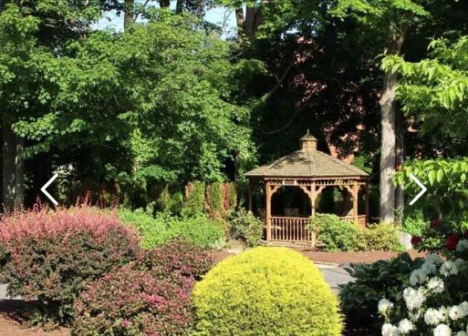 A peaceful garden scene featuring a wooden gazebo surrounded by lush greenery.