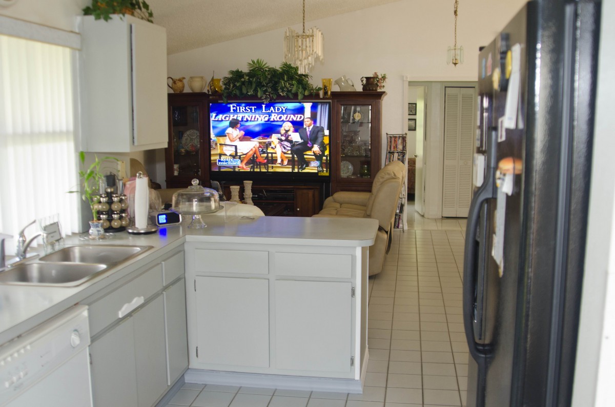 An open kitchen area leading into a living room with a large television.