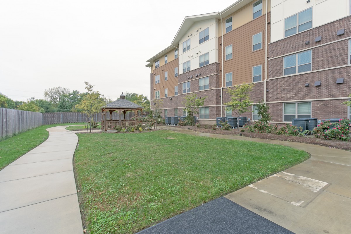 A view of an apartment building with a well-maintained lawn and surrounding walkway.