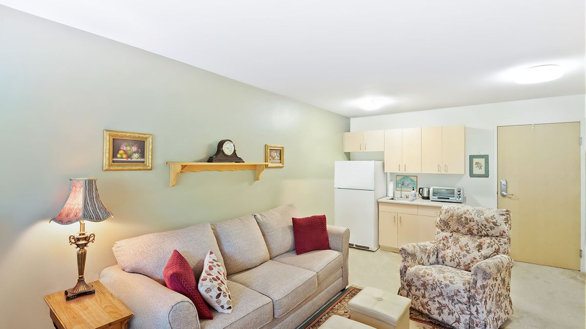 A cozy living room with a sofa, cushions, and a kitchenette in the background.