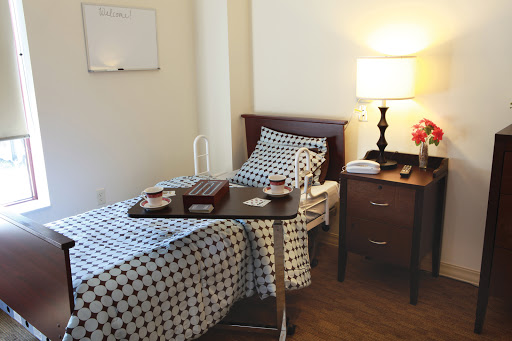 A neatly arranged hospital or care room featuring a bed, bedside table, and warm lighting.