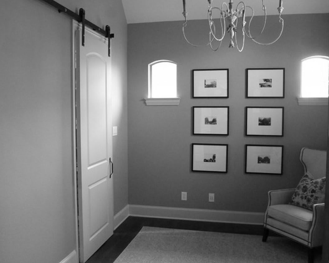 A cozy bedroom featuring a barn-style sliding door, a small window, a chandelier, and neatly arranged framed pictures on the wall.