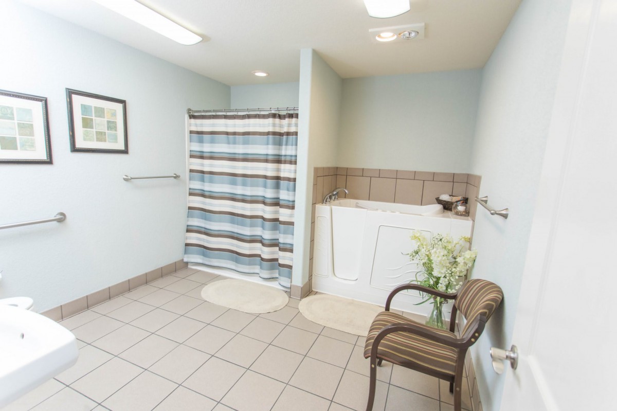 A clean and spacious bathroom featuring a shower with striped curtains, a sink, and a chair on a tiled floor.