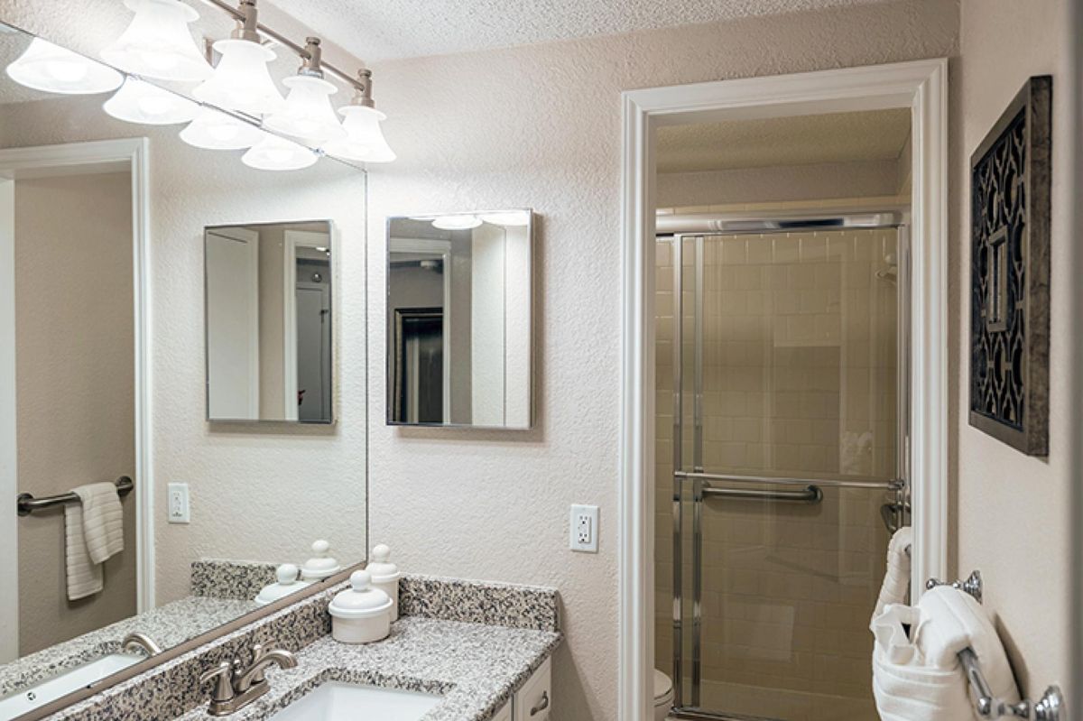 A modern bathroom featuring a granite countertop, double mirrors, and a glass-enclosed shower.