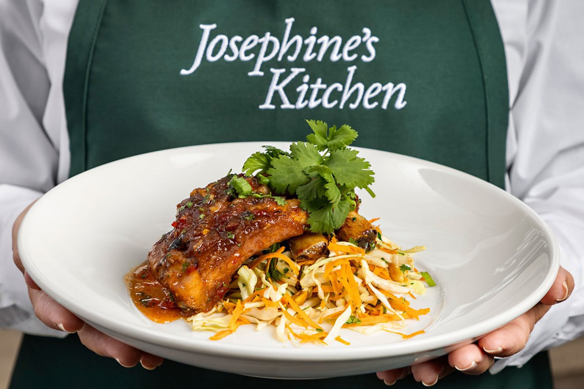 A deliciously plated dish from Josephine's Kitchen featuring salmon on a bed of seasoned vegetables.