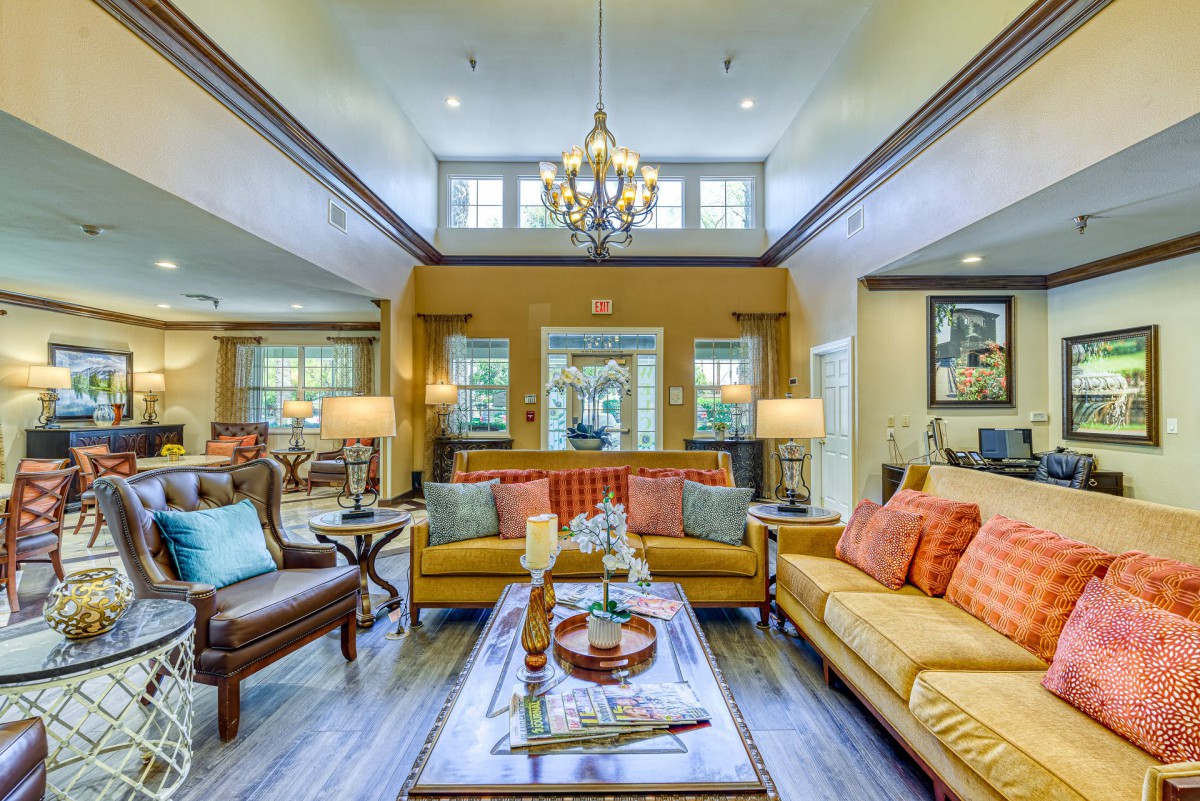 A spacious and elegantly designed living room with colorful sofas, a central coffee table, and a chandelier hanging from the ceiling.