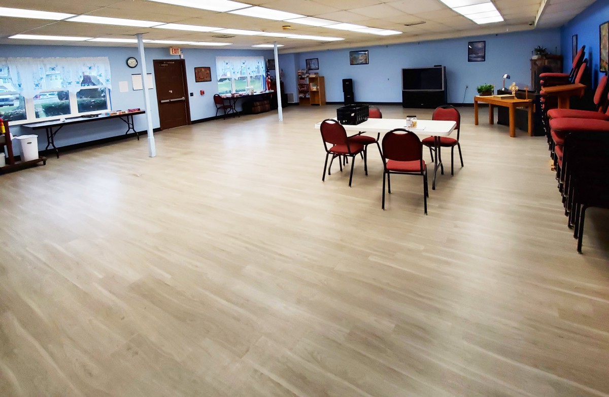 A spacious community center room with tables and chairs arranged for a meeting.