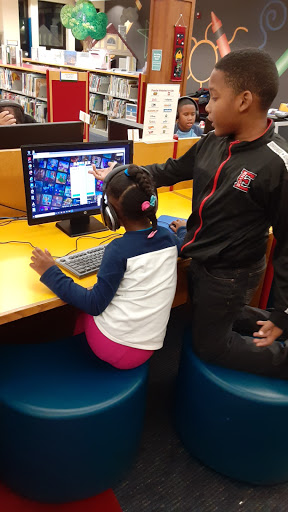 Two children engaged with a computer in a library setting.