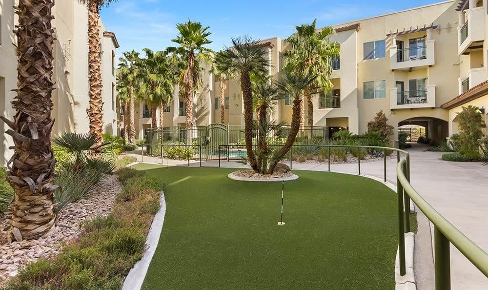A modern apartment complex featuring a landscaped outdoor area with a putting green and palm trees.