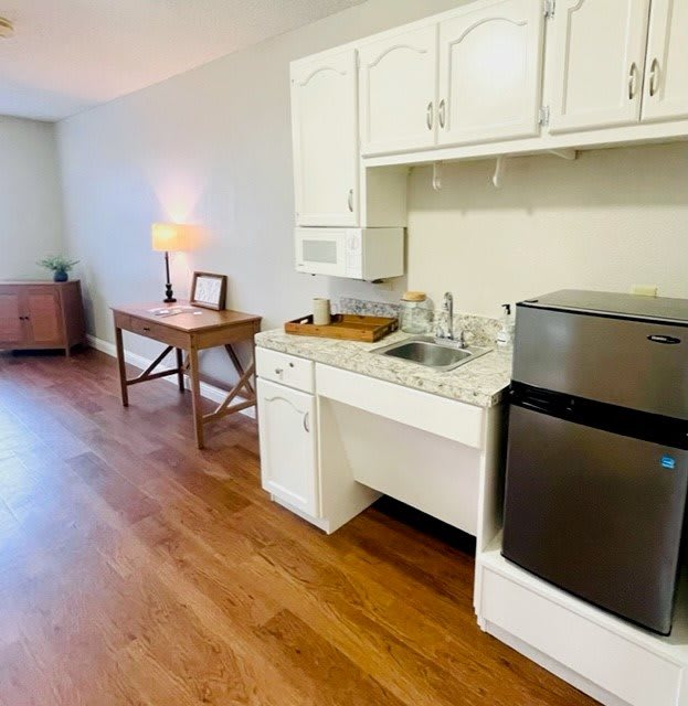A compact kitchen area with white cabinets, countertop appliances, and a wooden floor.