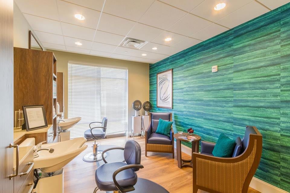 A modern salon interior featuring stylish chairs, a green accent wall, and bright lighting.